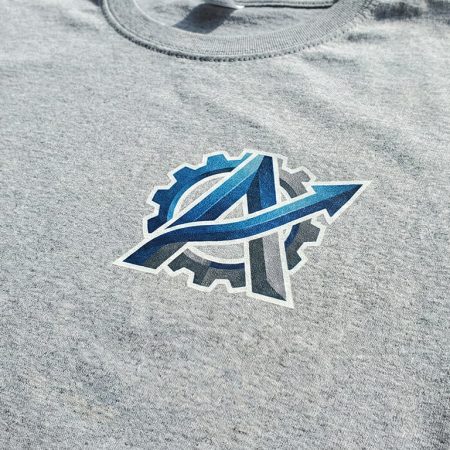 Graues T-Shirt mit mehrfarbigem Firmenlogo (Zahnrad und Pfeil) im DTF-Digitaldruck – Textilveredelung mit Farbverläufen.