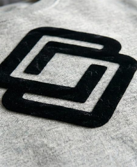 Samtiger Flockdruck in Schwarz auf einem grauen Sweatshirt – Detailaufnahme der edlen, erhabenen Haptik für hochwertige Textilveredelung.