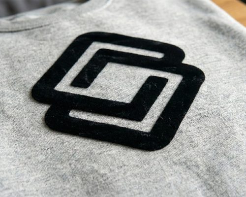 Samtiger Flockdruck in Schwarz auf einem grauen Sweatshirt – Detailaufnahme der edlen, erhabenen Haptik für hochwertige Textilveredelung.