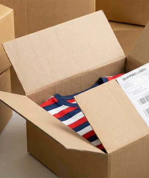 Versandkarton mit T-Shirt wird für den Versand etikettiert, Print on Demand und Fulfillment Service für Onlineshops.