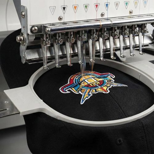 Industrielle Stickmaschine bestickt eine schwarze Cap mit einem mehrfarbigen Firmenlogo. Beispiel für hochwertige Bestickung von Caps in Bad Dürkheim.